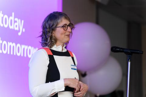 Woman with glasses talking at microphone.