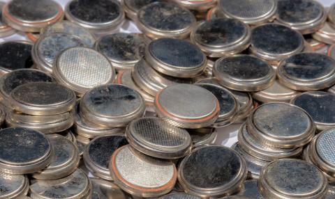 A pile of old button batteries for recycling. The batteries are the type used in desktop computers. They are old and dirty. Slight rainbow effect (colors) is caused by the way light is reflected from the batteries (it is not noise). Focus is on the closer batteries.