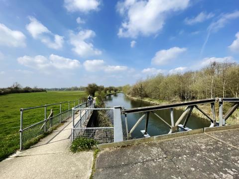 Riverbank and bridge beside a field.