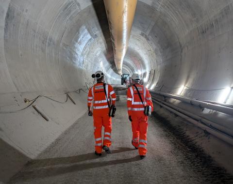 Two workers in orange high vis protective workwear walking through tunnel