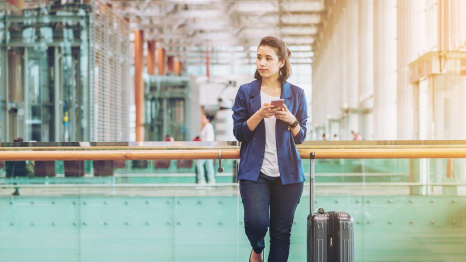 Stock image of business woman holding a cell phone in an airport with suitcase