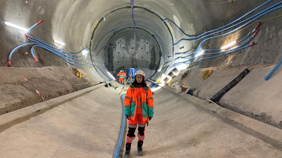 Woman in hard hat and orange work suit standing in giant tunnel