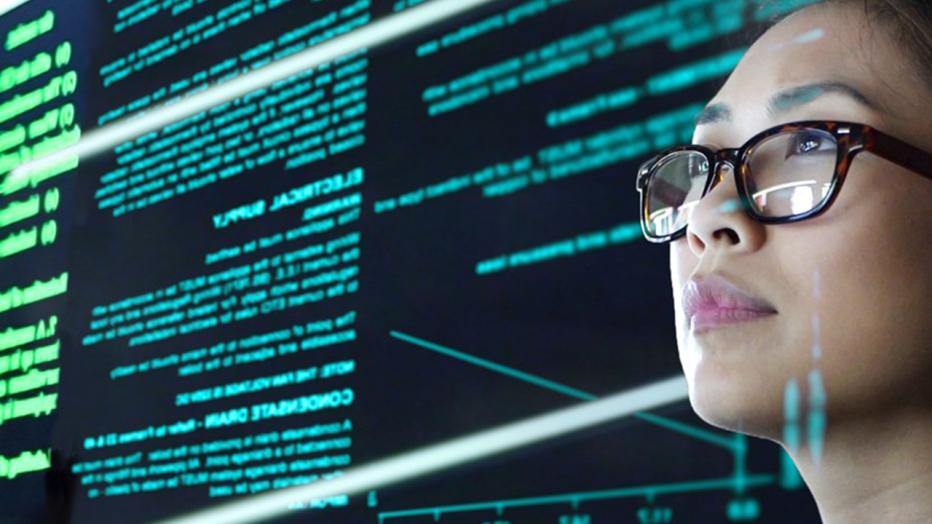 Asian woman in glasses looks at a screen full of data