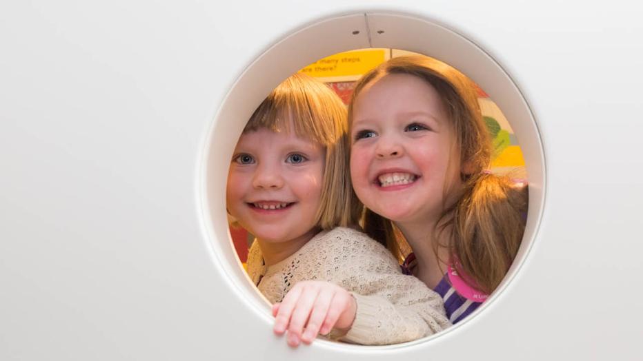 Two blond children look through a circle at a museum 