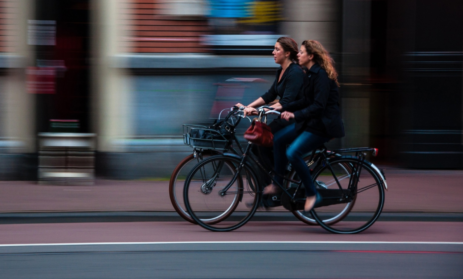 Two women riding bikes on a blurred street