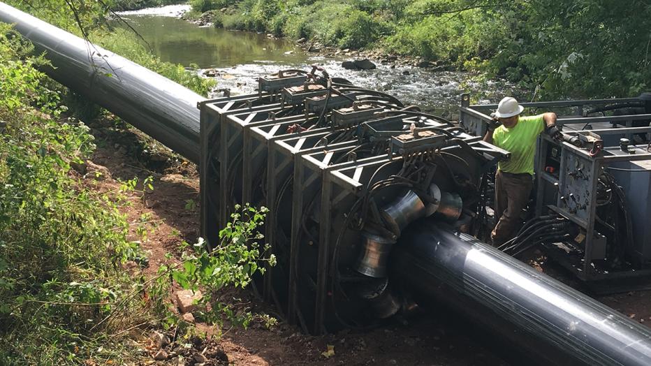 Engineer in neon yellow shirt and white hard hat works on a water pipeline