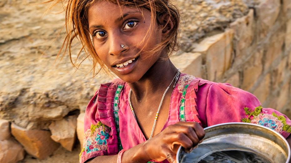 Black child in colorful dress carrying water