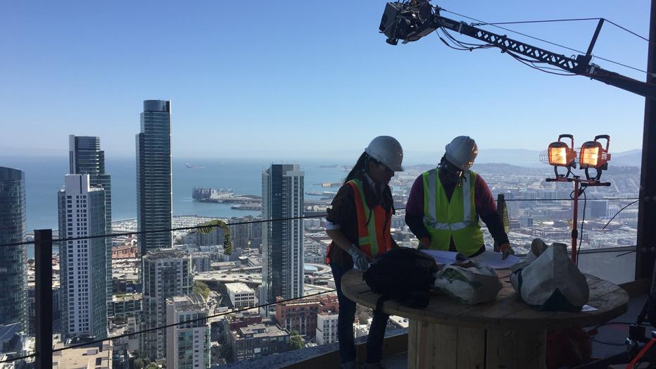 Engineers in hardhats at top of skyscraper with skyline behind them