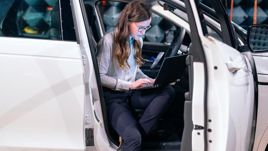 woman sitting in driver's seat with door open looking at laptop