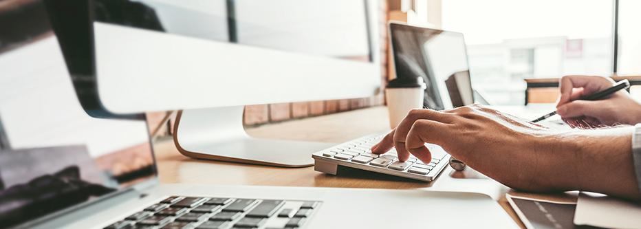 Man typing at a desktop Mac computer with a laptop and IPad nearby