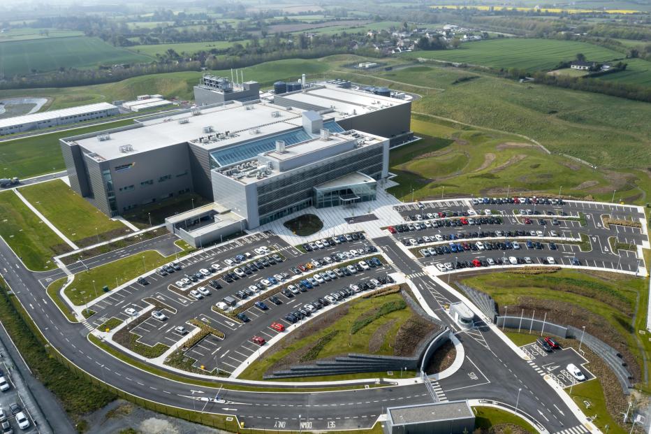 Aerial image of a white office building and parking lot surrounded by green hills