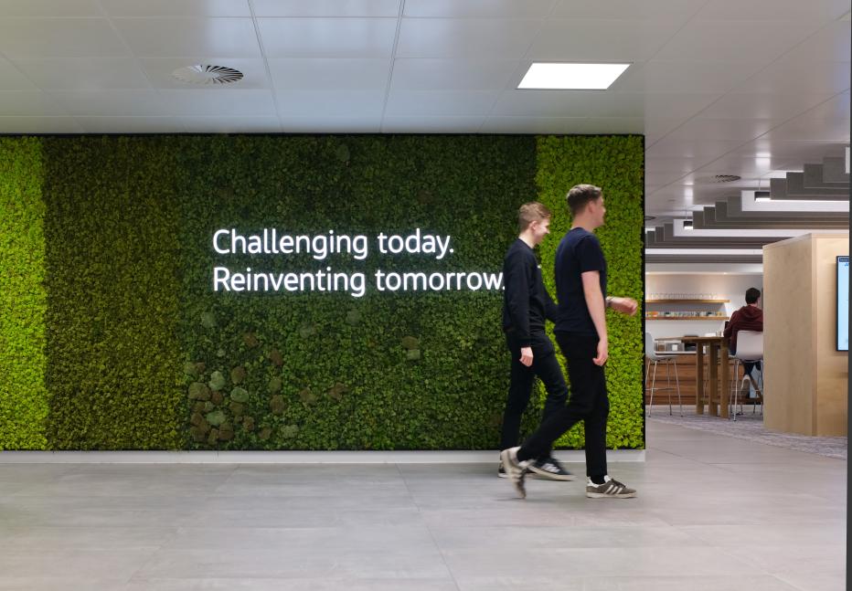 Two men walking past green wall in office area