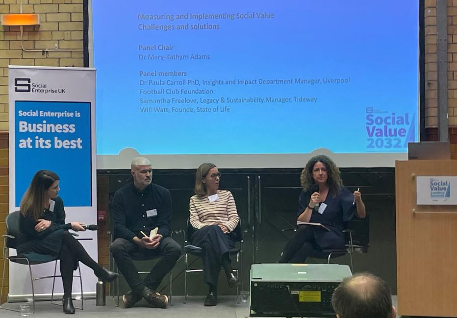 Four people in a panel discussion seated on a stage in front of a screen.