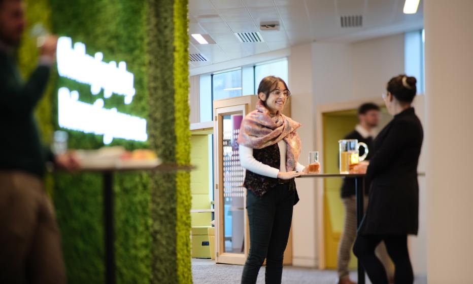 Jacobs women in an office talking in front of a green moss wall