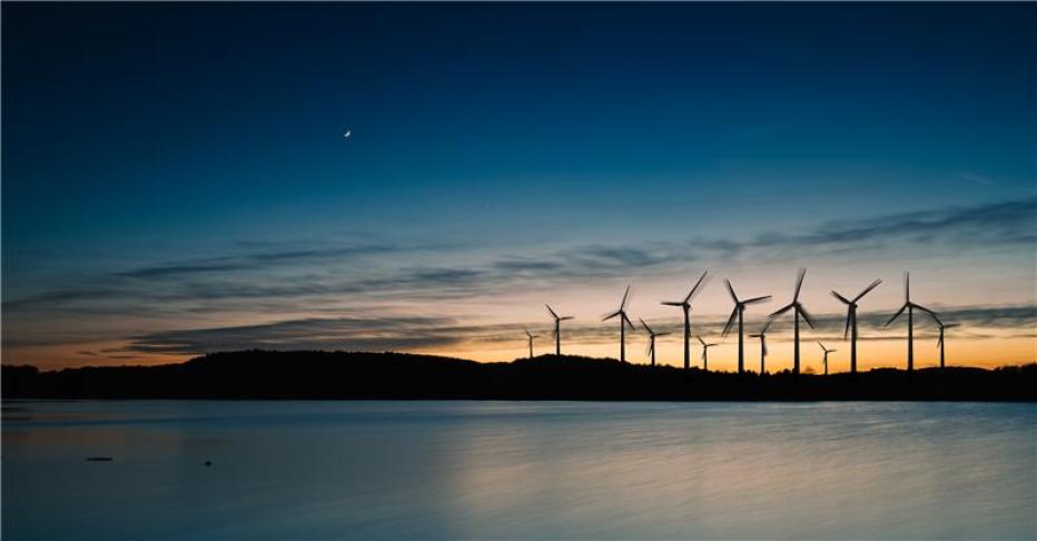 Twilight landscape with wind turbines silhouetted against a colorful sky and reflected in calm water