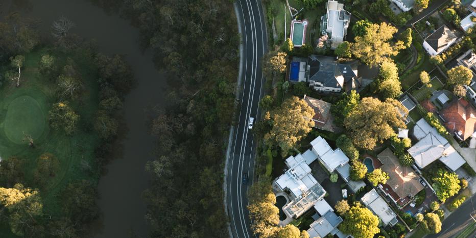 Aerial view of a suburban neighbourhood bordered by a forest, with a winding road separating homes from dense greenery