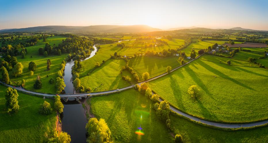 Aerial panorama over idyllic countryside green fields mountains golden sunset