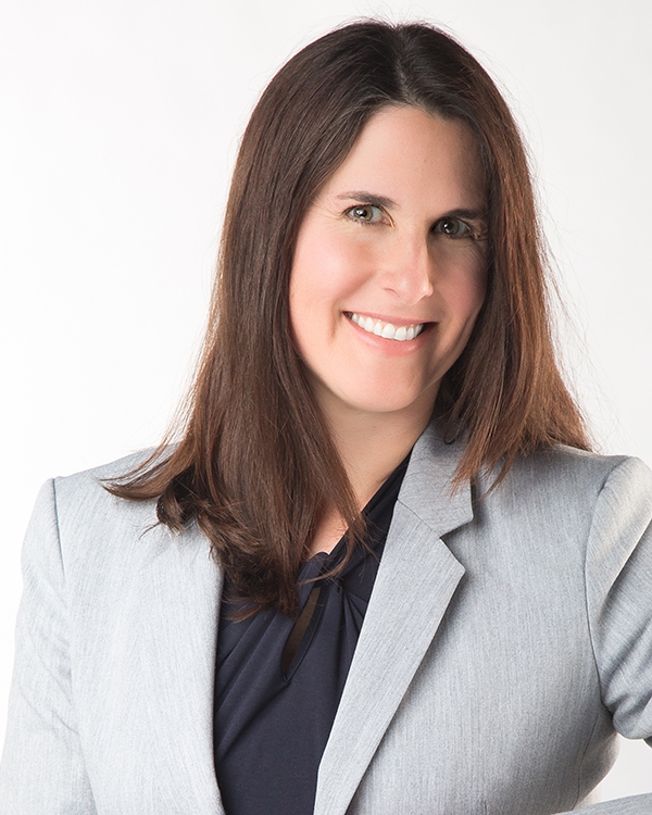 Head‑and‑shoulders studio portrait of a person in a light gray blazer over a dark top, photographed against a plain white background.