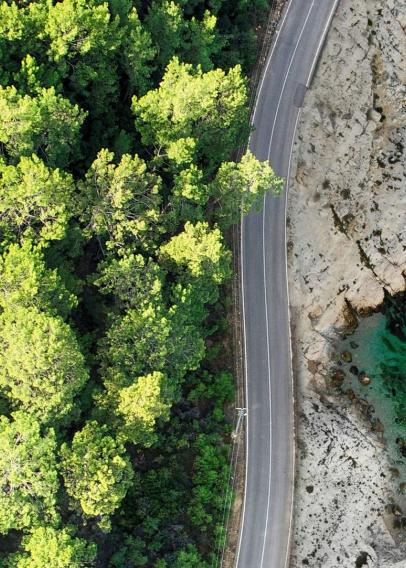 Aerial view of a road cutting in between green trees and bright aqua body of water