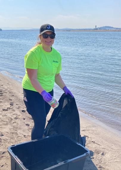Woman in neon tshirt and purple gloves picking up trash on a beach