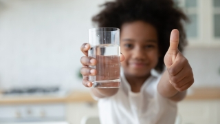 Hands holding glass with fresh pure water and showing thumbs up gesture
